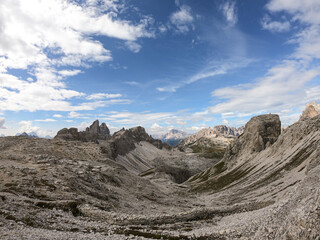 A panoramic view on a high and desolated mountain peaks in Italian Dolomites. The lower parts of the mountains are overgrown with moss and grass. Raw and unspoiled landscape. A bit of overcast.