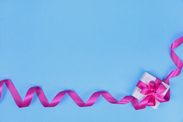 The gift box is tied with pink ribbon on a blue background. Concept for Valentine's Day, Women's Day, Birthday. Flat lay, top view, copy space.