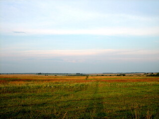 A flat horizon line between the sky and the earth. The sky and clear field in the countryside are illuminated by the rays of the setting sun.