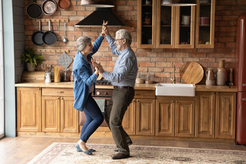 Full length energetic middle aged family couple dancing to disco music in kitchen. Happy old mature...