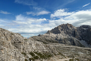 A panoramic view on a high and desolated mountain peaks in Italian Dolomites. The lower parts of the mountains are overgrown with moss and grass. Raw and unspoiled landscape. A bit of overcast.
