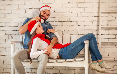 Happy in love couple in red Santa hats on white background brick wall in room