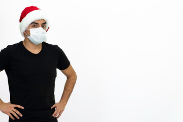 Fototapeta premium Young male wearing a medical face mask and a santa hat. Young man is holding a heart-shaped gift box in his hands. Isolated image and white background.