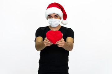 Young man wearing a Santa hat. She is holding a heart-shaped box in her hand, wearing a medical face mask.