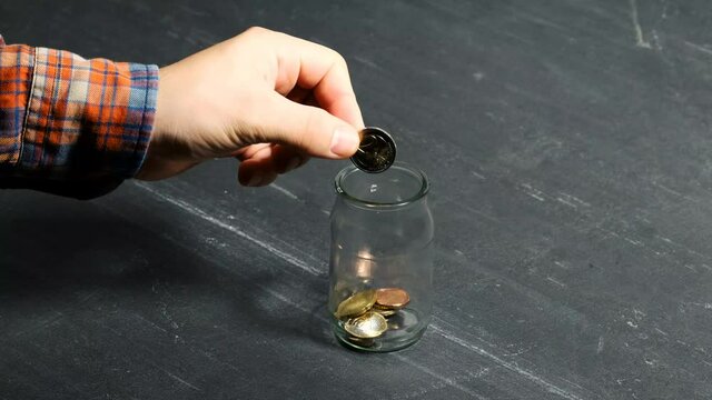 A two-euro coin is placed in a jar with other euro coins for saving by a man's hand on a black background. The covid pandemic crisis is forcing people to save money. Stay safe and save money.