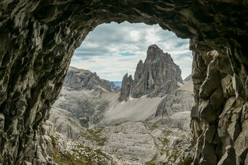 Fototapeta na wymiar A view from a cave on distant and high mountain chain in Italian Dolomites. The mountains are steep and dangerous, with a lot of lose stones. Discovering and experiencing. Overcast