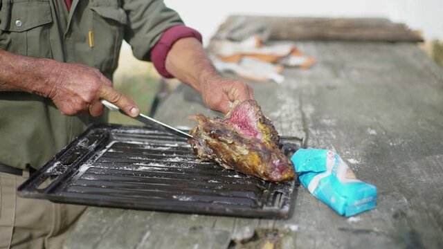 Hands cutting a piece of meat on the grill, very rustic.