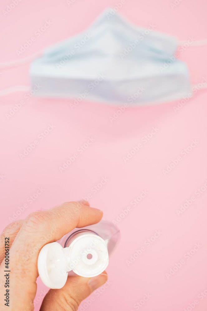 Poster Vertical shot of a hand sanitizer alcogel and a surgical mask isolated on pink background