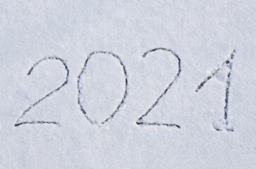 The numbers 2021 are written on snow. Finger lettering on snow 2021. New Year's date concept. Coming 2021 year outlined on the snow winter background. Inscription 2021 on the snowdrift 