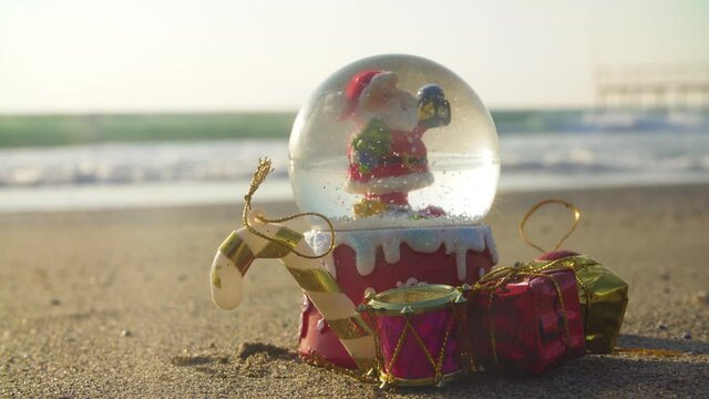 Christmas snow ball globe on the beach, by the sea as a symbol of christmas resort