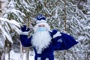 Father Frost in a disposable mask with a bag of gifts in a snowy forest. Christmas character of Russia Father Christmas. Social distance, protection against coronavirus.