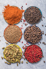 mix of aromatic coriander, black, red peppercorn,  paprika in white cups on gray concrete background Top view Flat lay Healthy food. Bowls with various spices on white background