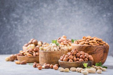 Assortment of nuts in a wooden bowls, on a gray background. Hazelnuts, pistachios, almonds, brazil nut, cashews