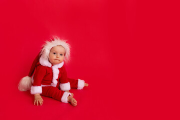 a small child of six months in a Santa costume sits on a red isolated photophone, a place for text, the concept of the new year and holiday
