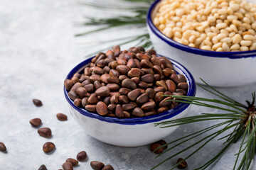 Cedar nuts unshelled with cedar nuts shelled close-up. Cedar products: cedar oil in glass bottle, pine nuts, cone, brunches on a wooden broun background. Top view.