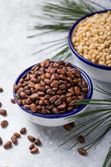 Cedar nuts unshelled with cedar nuts shelled close-up. Cedar products: cedar oil in glass bottle, pine nuts, cone, brunches on a wooden broun background. Top view.