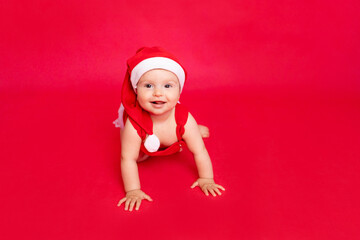 happy little baby six months old in Santa hat crawling on red isolated photophone, space for text, new year and holiday concept