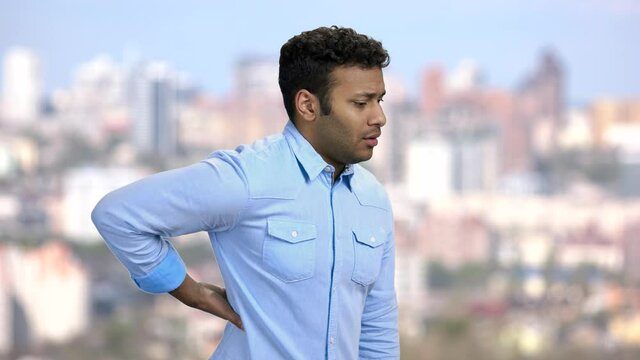 Office worker having sudden back ache. Young businessman suffering from strong back pain. Blurred city background.