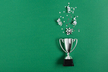 Winner or champion silver trophy cup with confetti on green background top view.