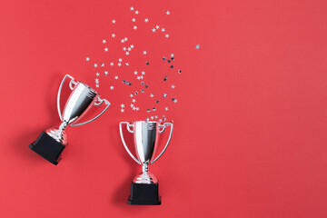 Winner or champion silver trophy cups with confetti on red background top view.