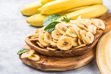 Homemade Dehydrated Banana Chips in a Bowl and fresh banana and slices on table