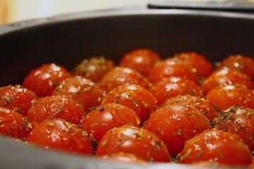 Cooking red cherry tomatoes with olive oil, fine herbs and honey in the oven, homemade food in the pan on the kitchen table.
