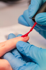 close-up of a woman applying red nail polish. Women's beauty service