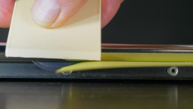 Close POV shot of a man&rsquo;s hand inserting a piece of thin yellow card onto the surface of an office paper trimmer, then running the rotary blade horizontally across the card to cut off a straight edge.