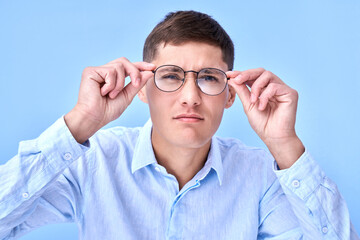 Studio shot caucasian man with poor eyesight holds hands on the rim of glasses and squints, trying...