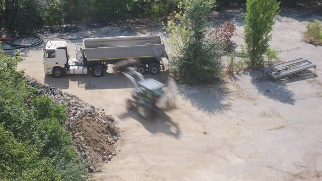 Loader vehicle loads asphalt debris into dump truck, under windy conditions. Timelapse, construction site.