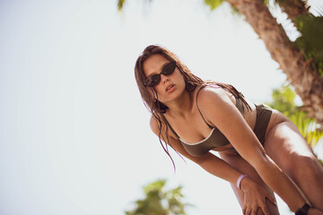 cute young teenage girl or woman posing and having fun on the beach under palm trees in summer swimsuit . Trendy girl posing. Funny and positive woman in sunglasses