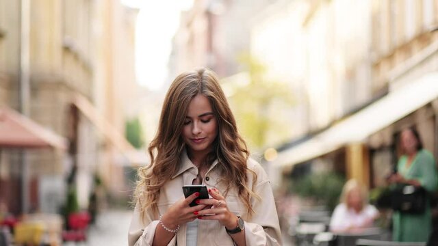Portrait of attractive woman texting message on smartphone on city street in slow motion