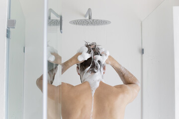 Rear back view young caucasian man washing hair with moisturizing foamy natural shampoo or gel under runny water, enjoying every day body cleansing routine, taking morning shower in bathroom.