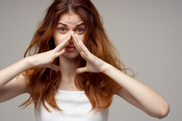woman with loose hair touches her head with hands white t-shirt gray background