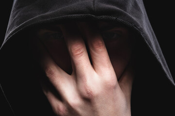 Close-up low key portrait of a man in a hooded hand gesture makes a sperm hero mask. The concept of...