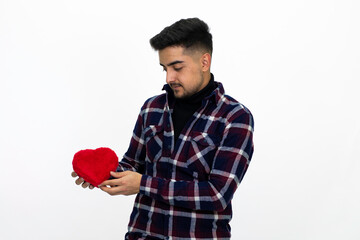 Handsome young male model. He is holding a gift box in the shape of a heart. He is wearing a dark checkered shirt.