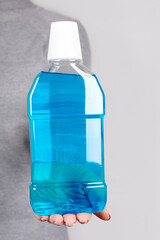 Hand with blue mouthwash on grey background.
