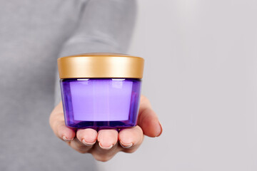Hand with purple cosmetic jar on grey background.