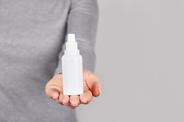 Hand with nasal drops on grey background.