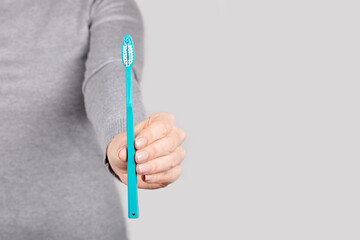 Hand with blue toothbrush on grey background.