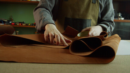 A professional Tanner corrects defects on a roll of genuine leather with a special wax. The process of creating a hand made product.