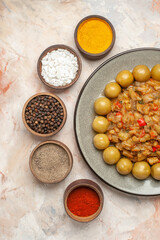 top half view roasted eggplant salad on plate different spices in small bowls on nude background