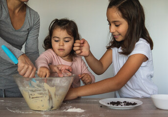 Two sisters prepare cookies with their mother