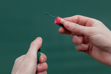 Man Lighting Up Firecracker in his Hand Against the Blue Background Using Gas Lighter
