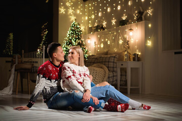 Couple in knit sweaters near Christmas tree. Man and woman in Christmas interior room.