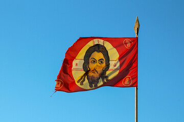 Orthodox red flag with a cross and jesus on a spear fluttering in the wind against the blue sky. Kozak symbol