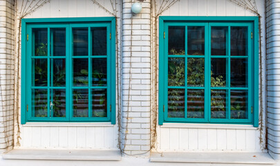 Two large turquoise windows on the veranda of a brick house.