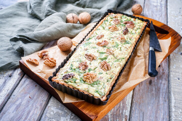 Traditional French Autumn walnut spinach tarte served as close-up in a backing form on an Modern design wooden board