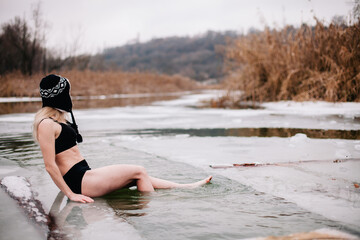 Young slender girl bathes in winter in a river hole