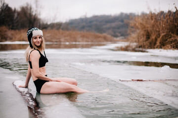 Young slender girl bathes in winter in a river hole